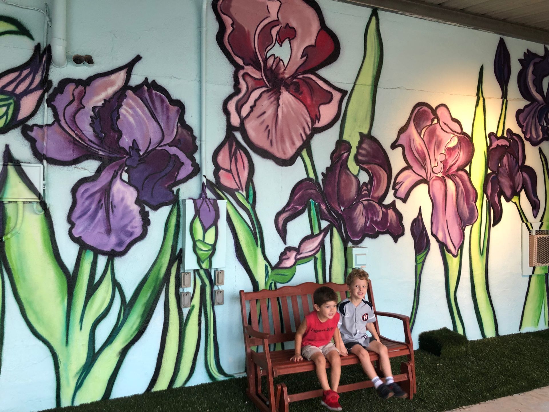 Two children on a bench in front of a mural of purple and pink irises.