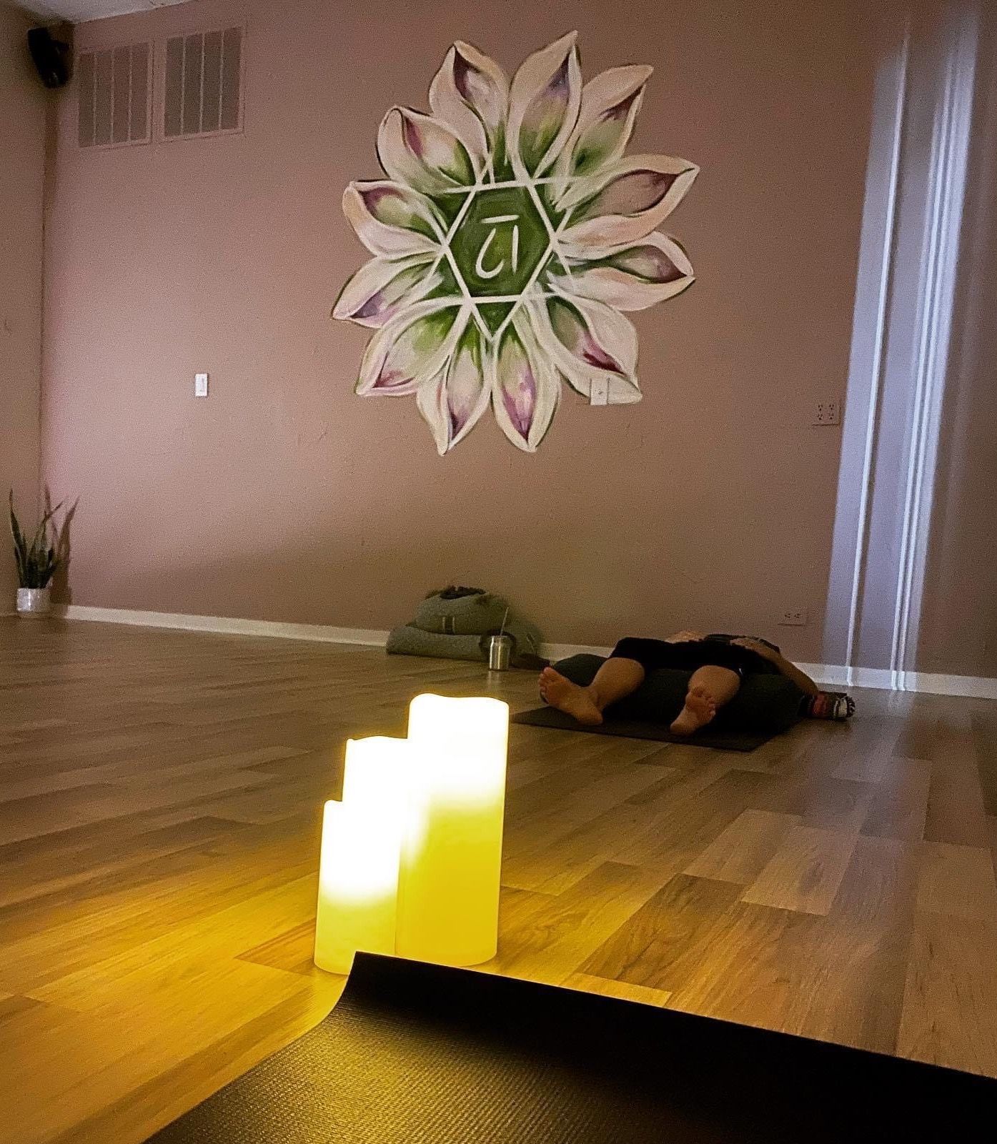 A yoga studio with candles, a floral wall art, and a person lying on a mat.