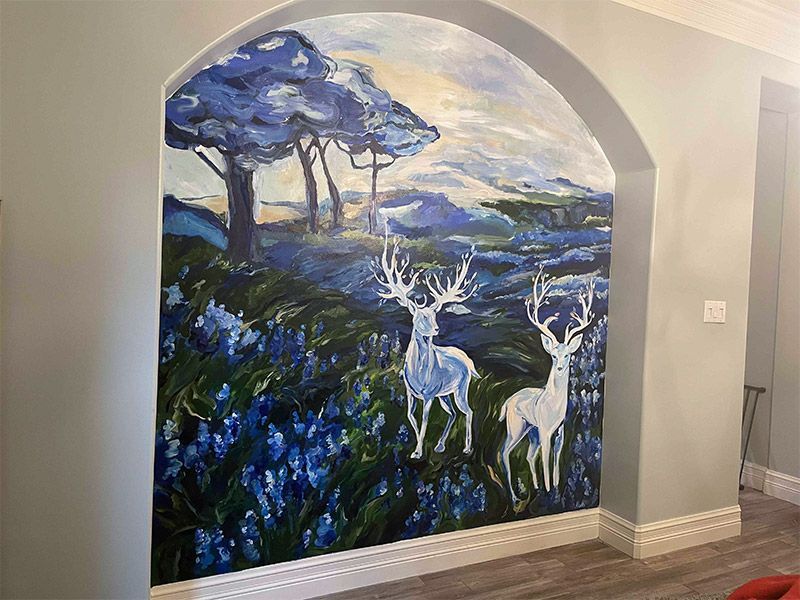 Mural of two white deer in a blue field, under blue trees, framed by an arched wall opening.