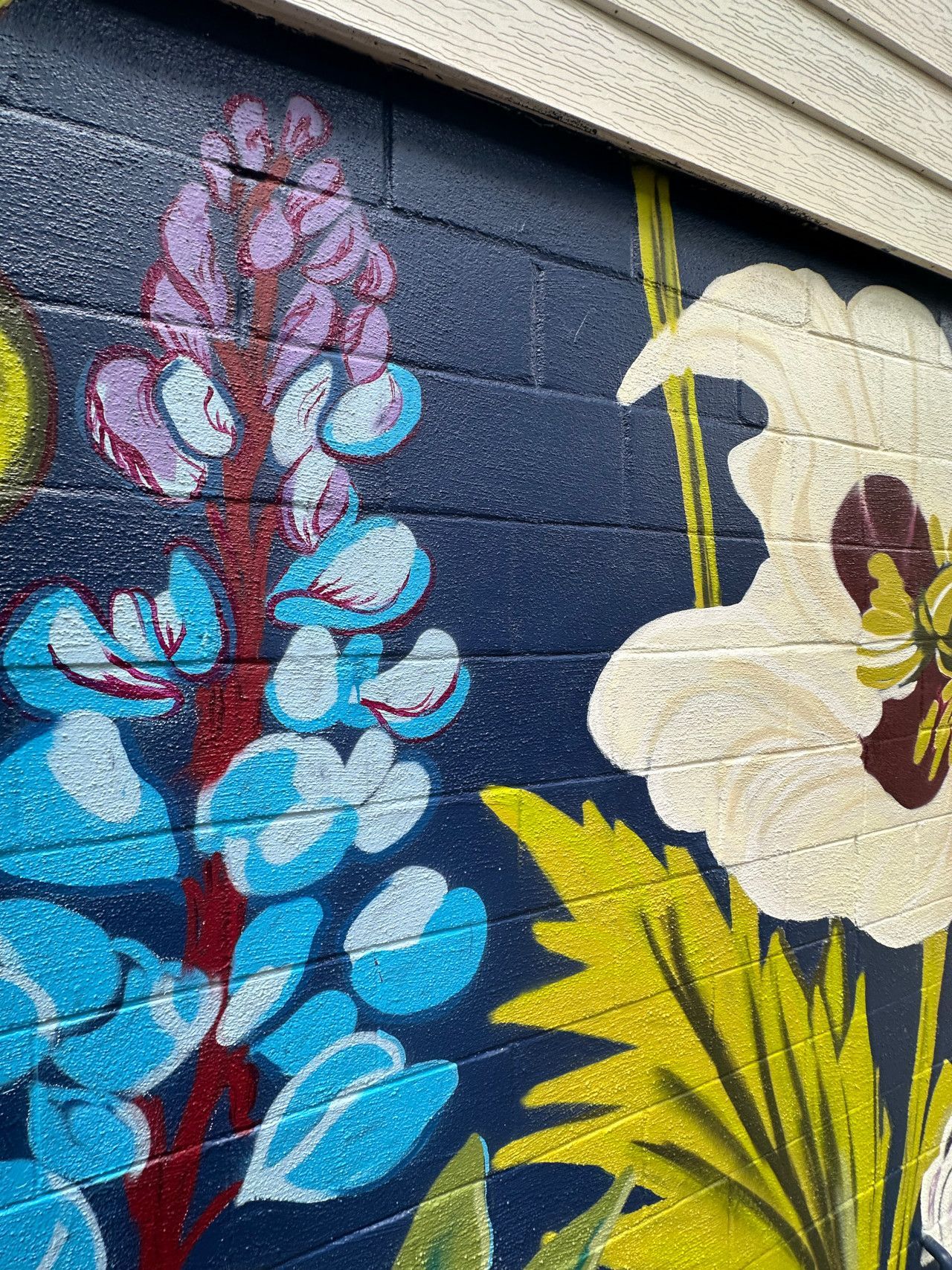 Mural of vibrant blue, purple, and white flowers on a dark blue brick wall.