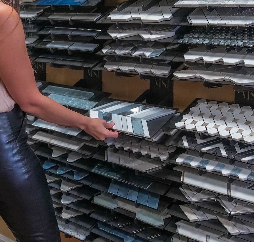 A woman is holding a stack of tiles in front of a shelf that has the letter m on it
