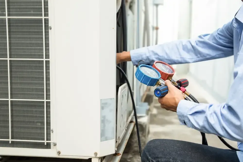 A man is working on an air conditioner with a gauge.