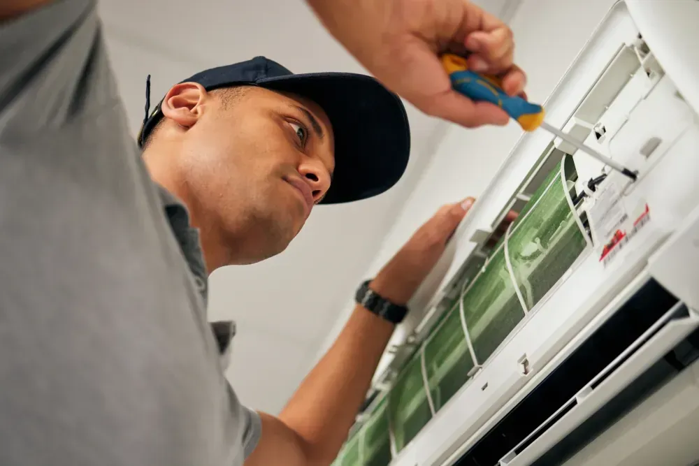 A man is fixing an air conditioner with a screwdriver.