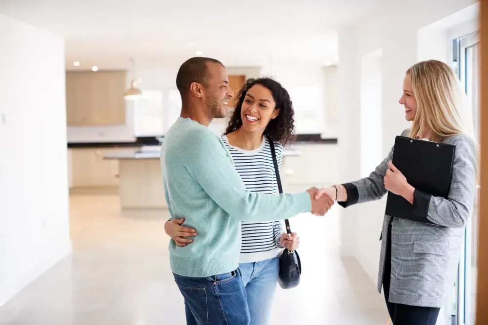 A man and woman are shaking hands with a real estate agent in an empty house.