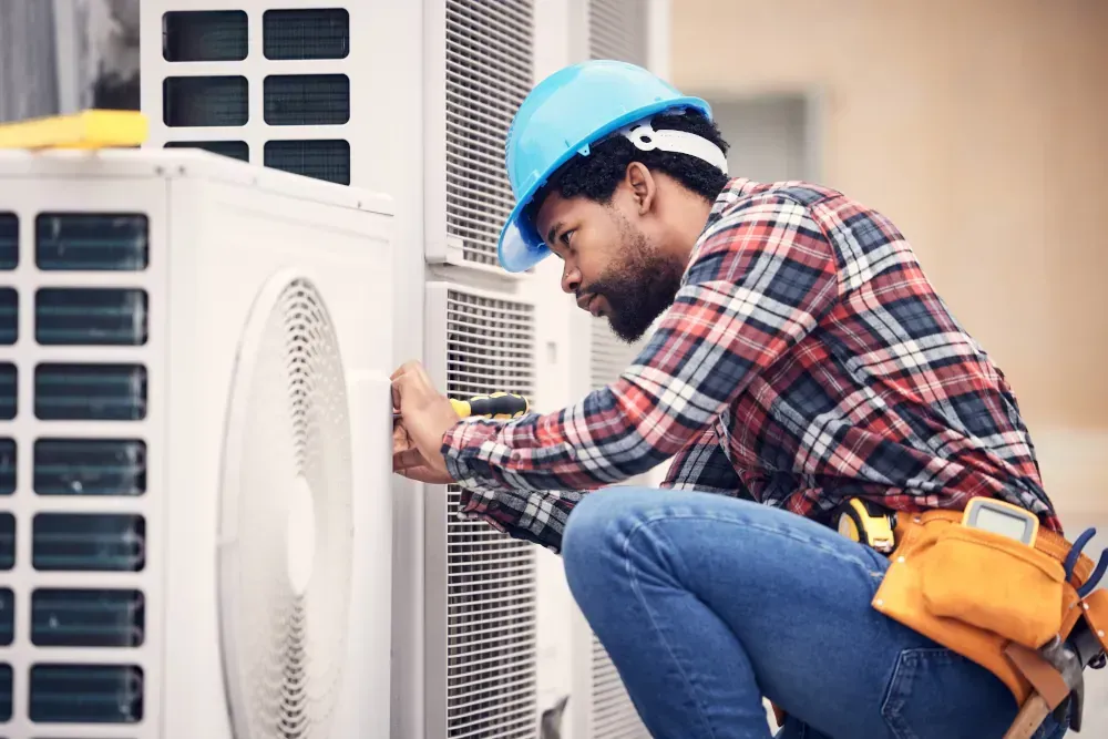 A man wearing a hard hat is working on an air conditioner.