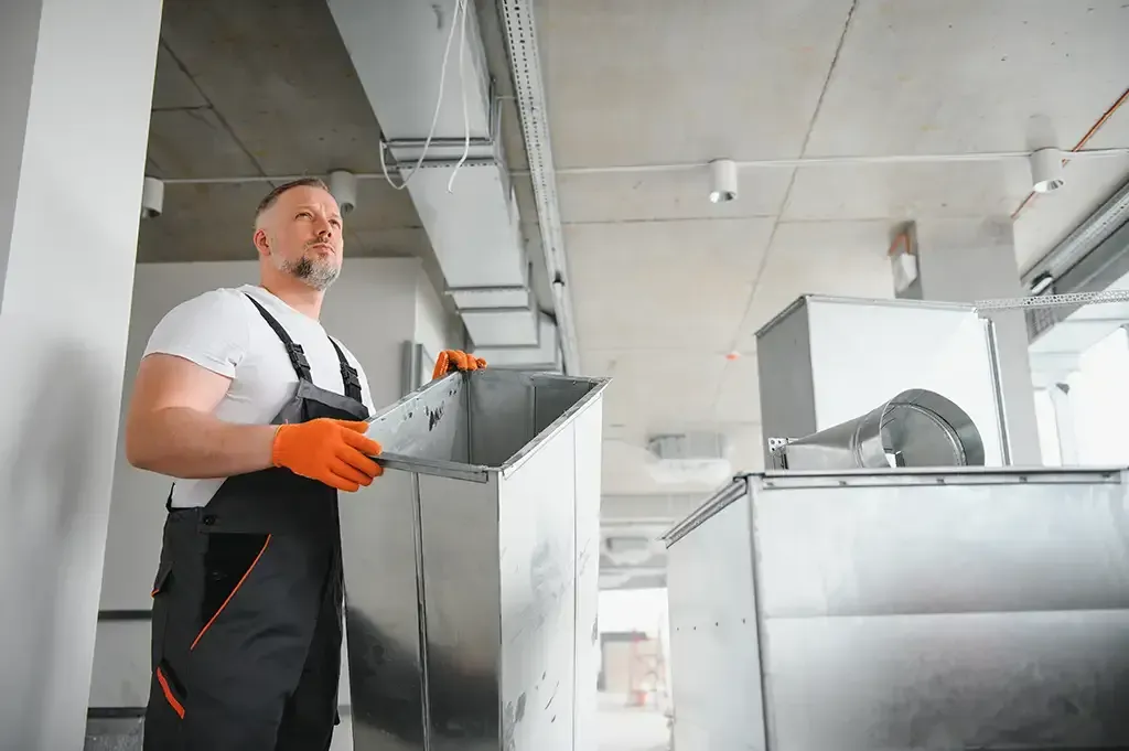 A man is working on a ventilation system in a building.