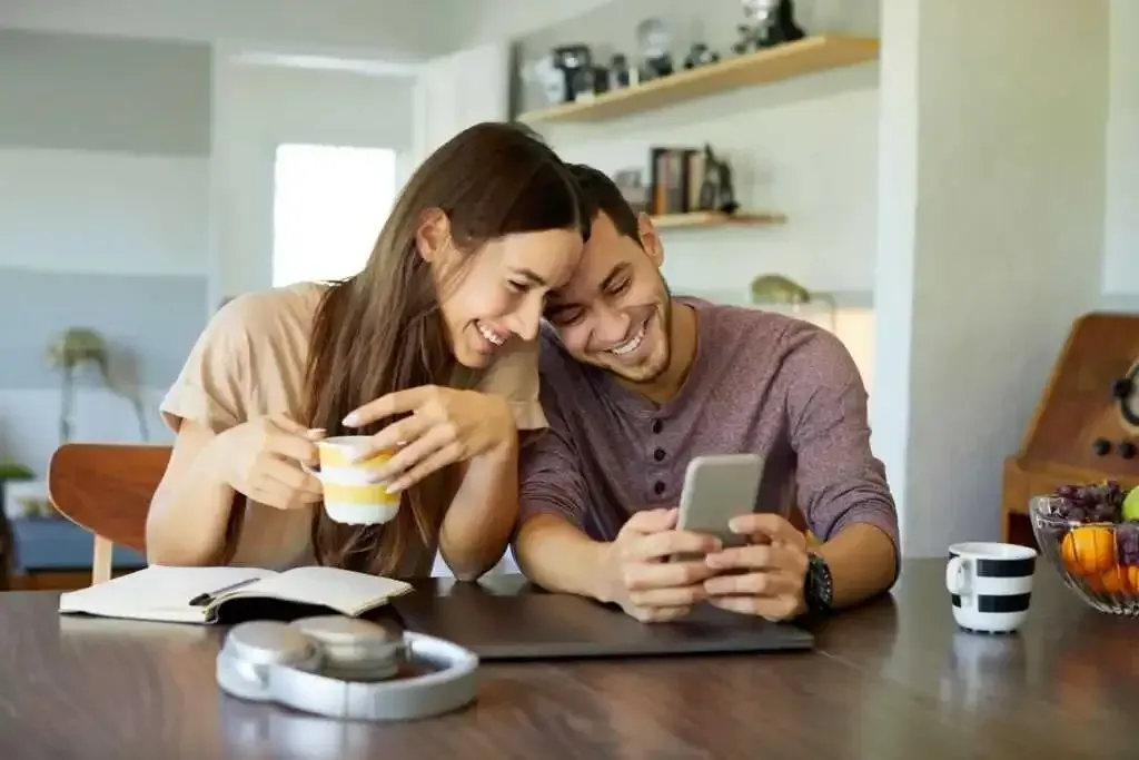 A man and a woman are sitting at a table looking at a cell phone.
