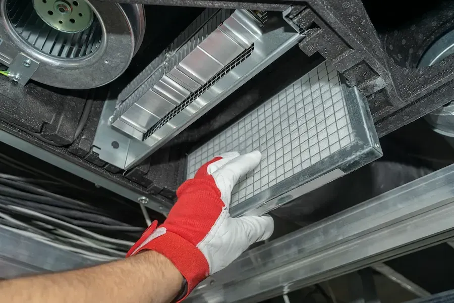 A person is holding a filter under a ceiling fan.