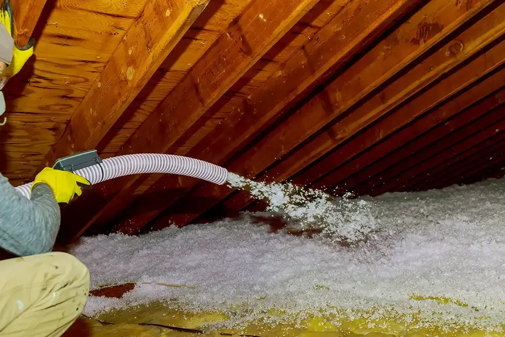 A man is blowing insulation into an attic with a hose.
