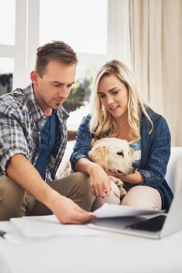 A man and a woman are sitting on a couch with a dog and looking at papers.