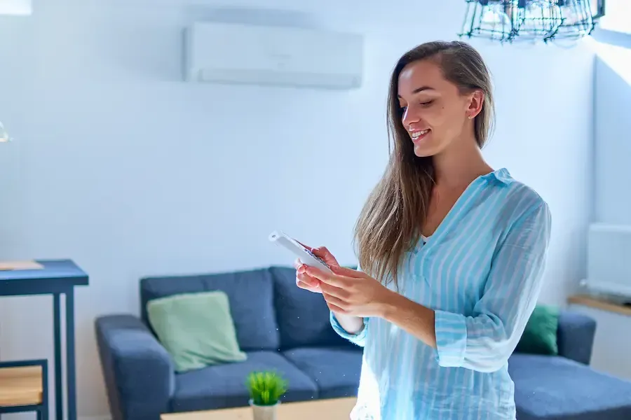 A woman is standing in a living room holding a cell phone.