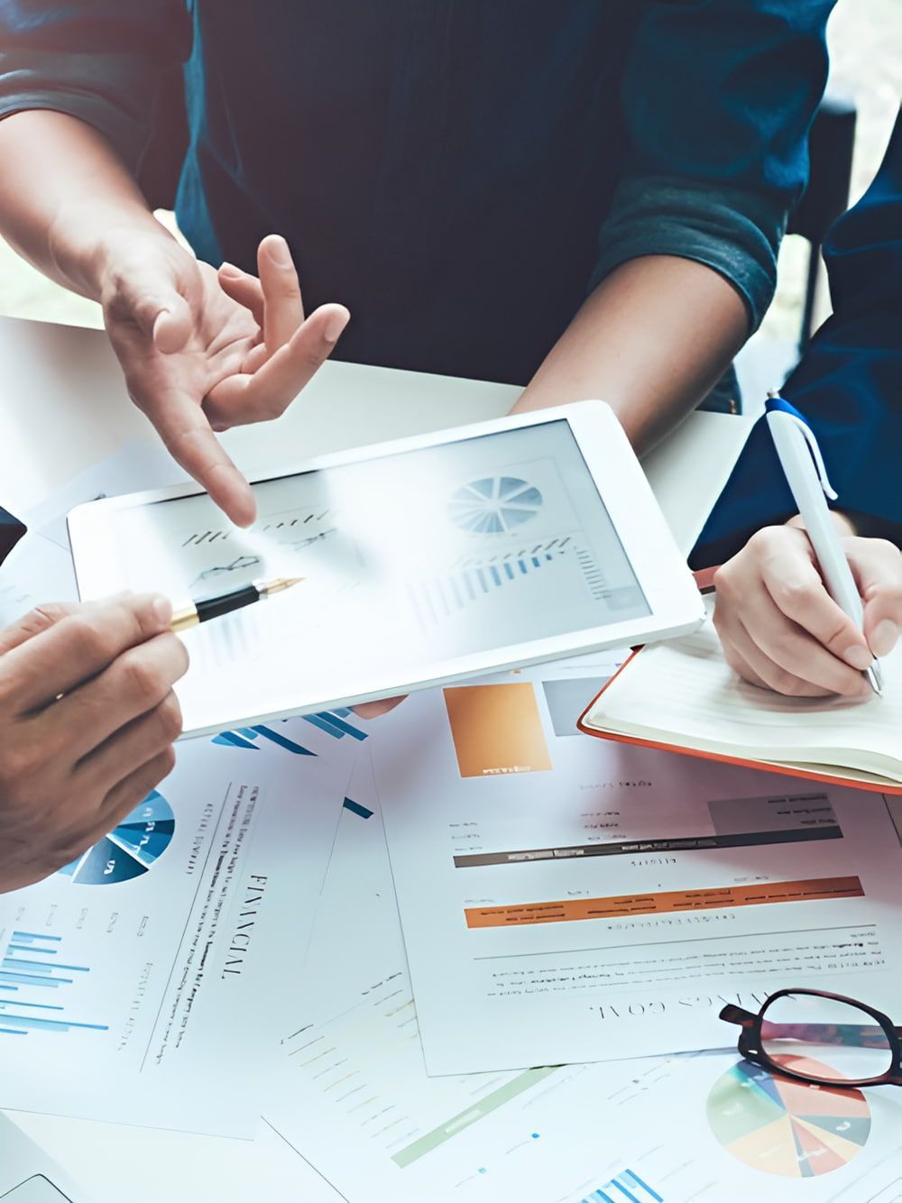 People Reviewing Financial Charts on a Tablet, Pointing and Writing — AJA Bookkeeping Services In Cooktown, QLD
