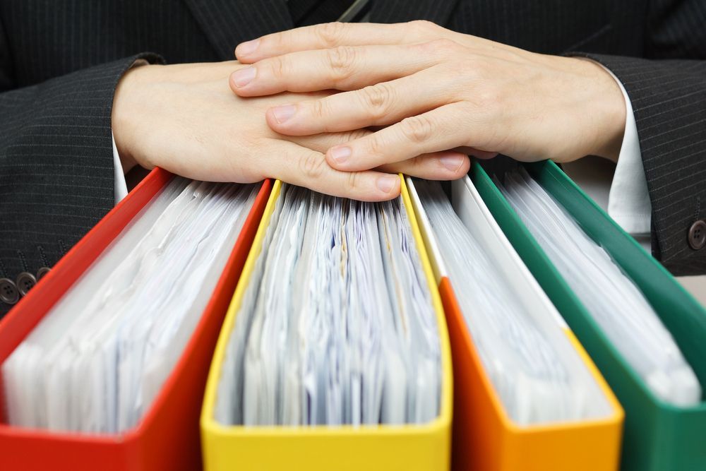 Person's Hands Rest Atop Red, Yellow, and Green Binders — AJA Bookkeeping Services In Hughenden, QLD