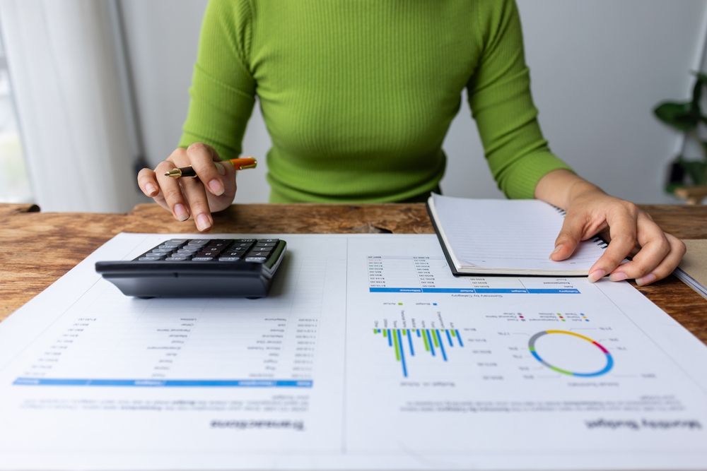Woman in Green Sweater Calculating Finances at a Wooden Desk — AJA Bookkeeping Services In Hughenden, QLD