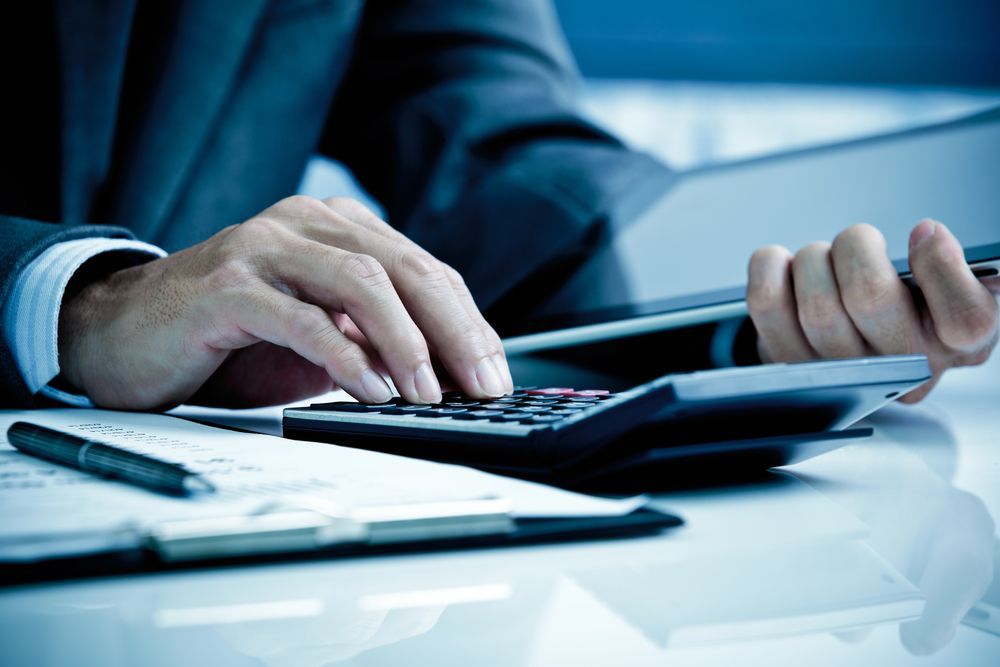 A Man in Suit Using Calculator on a Desk With Papers and a Tablet — AJA Bookkeeping Services In Karumba, QLD