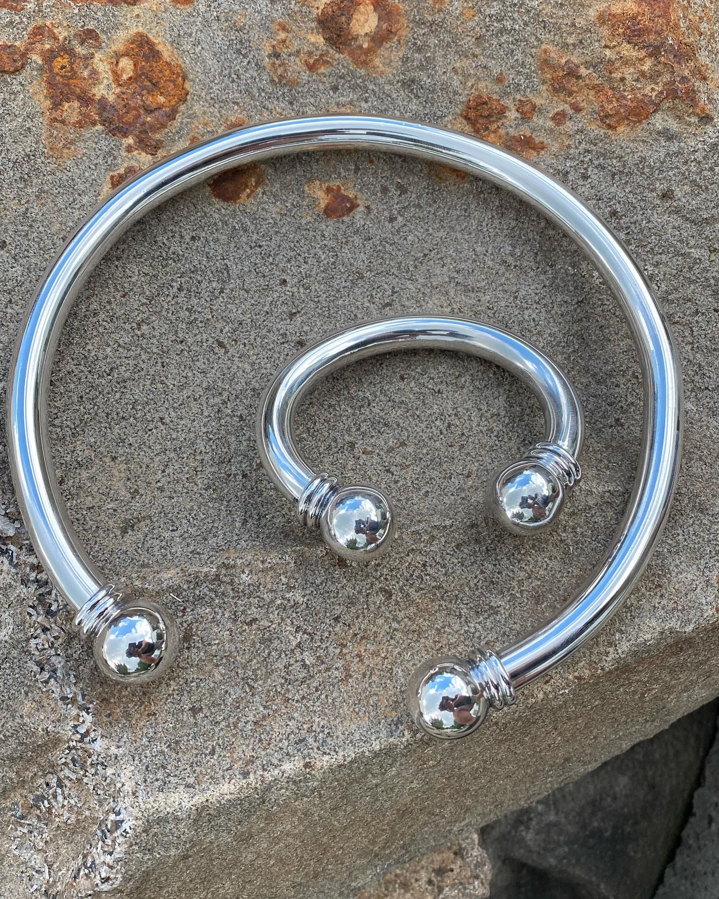 Two polished silver-tone cuff bracelets with spherical ends resting on a textured stone surface — Burchell's Jewellers In Bowral, NSW
