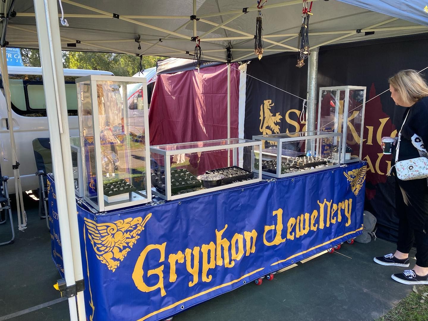 A Gryphon Jewellery stall at a market, featuring a blue banner, glass display cases with jewellery, and a person standing — Burchell's Jewellers In Bowral, NSW