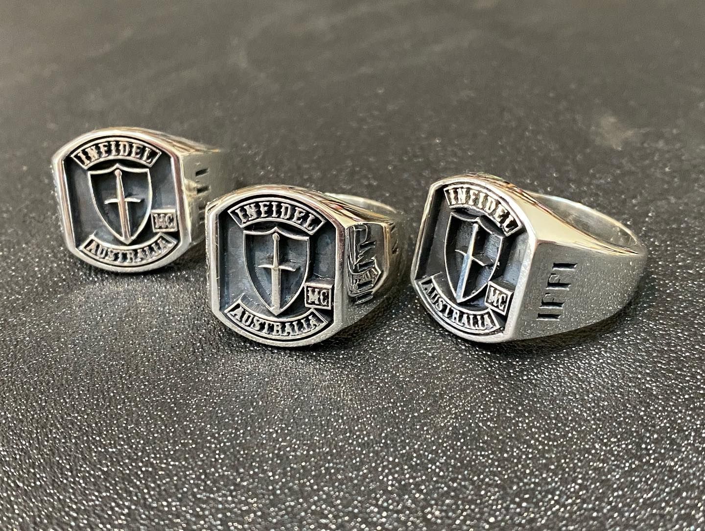 Three silver rings placed on a dark surface, each featuring a shield emblem — Burchell's Jewellers In Bowral, NSW