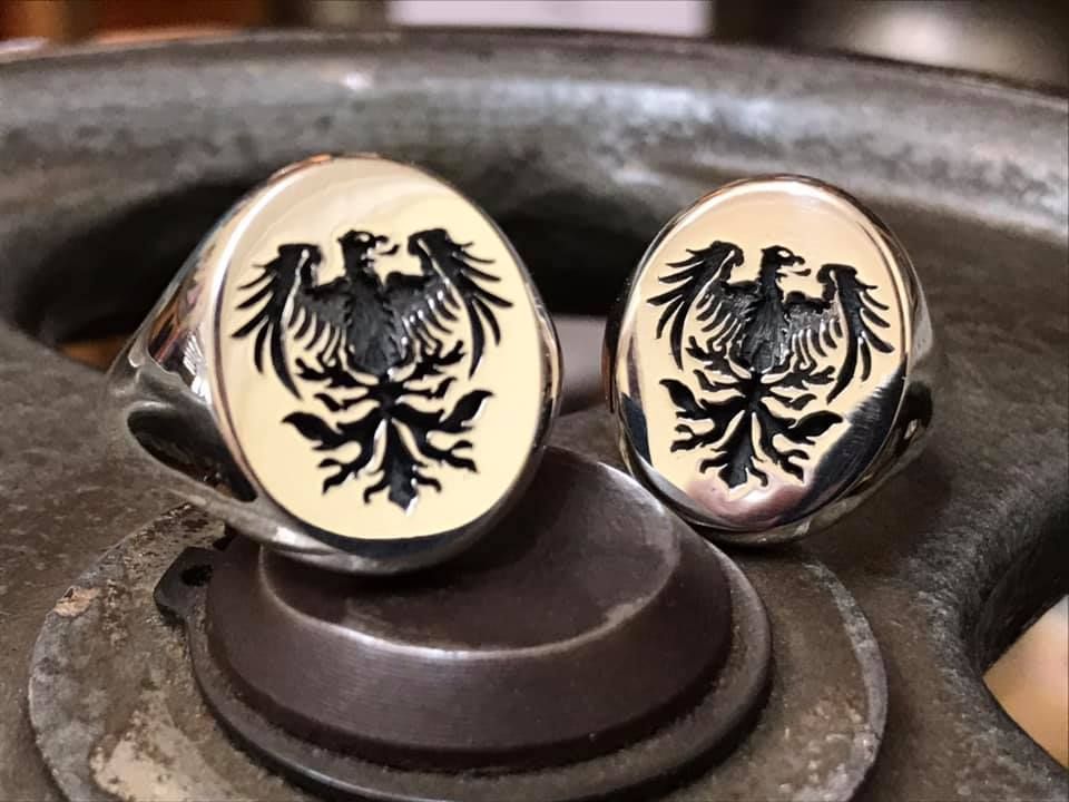 Two silver signet rings featuring an engraved black eagle crest resting on a dark metallic base. — Burchell's Jewellers In Bowral, NSW