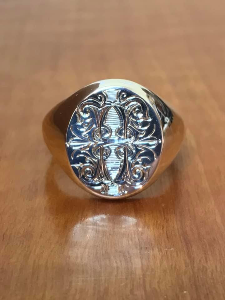 A gold signet ring with an oval face featuring an intricate, mirrored silver-toned scrollwork pattern — Burchell's Jewellers In Bowral, NSW