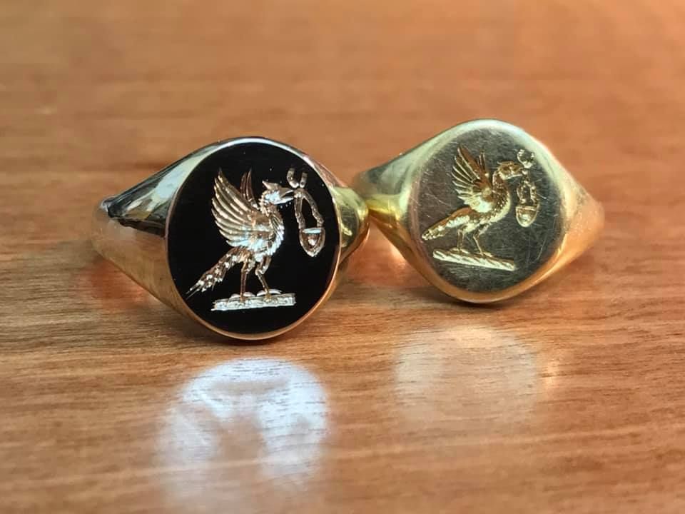 Two gold signet rings, one with a black inset and one plain gold, each engraved with a bird holding a twig — Burchell's Jewellers In Bowral, NSW