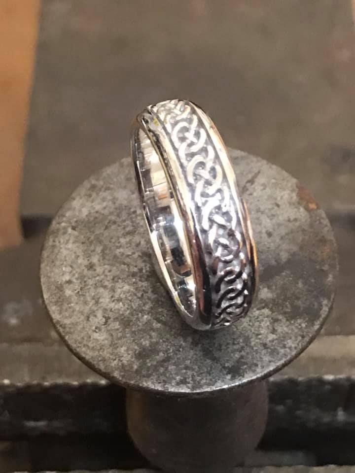 A silver ring with an intricate Celtic knot pattern, resting upright on a circular metal base — Burchell's Jewellers In Bowral, NSW