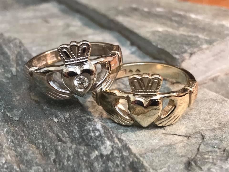 Two gold Claddagh rings, one with a small diamond in the heart, resting on a textured grey stone surface — Burchell's Jewellers In Bowral, NSW