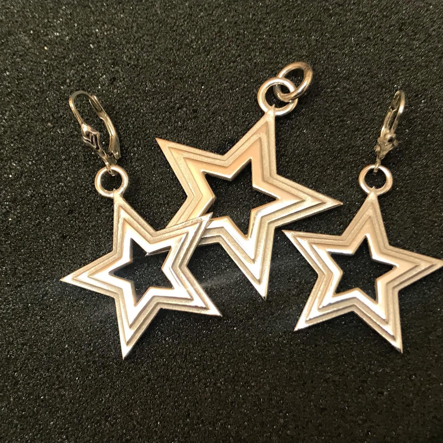 A set of three silver, star-shaped jewellery pieces—two earrings and a pendant—resting on a dark, textured foam surface — Burchell's Jewellers In Bowral, NSW