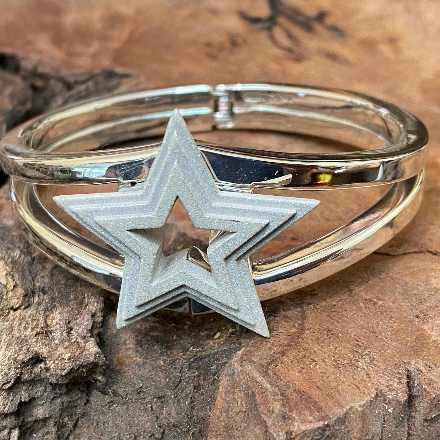 A silver hinged bracelet featuring a prominent, textured matte-silver star centrepiece resting against a wood surface — Burchell's Jewellers In Bowral, NSW