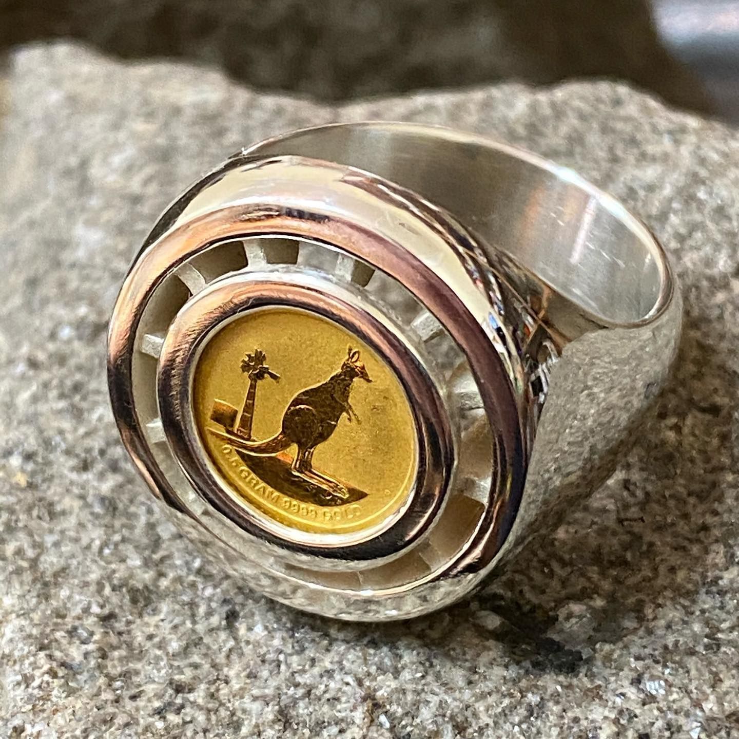 A silver ring featuring a small gold Australian kangaroo coin set in the center, displayed against a textured rock surface — Burchell's Jewellers In Bowral, NSW