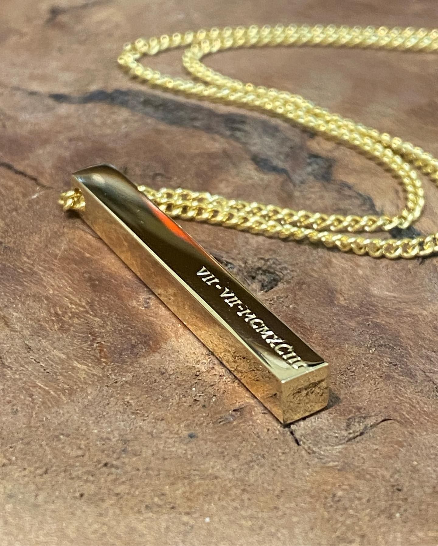 A gold bar necklace engraved with Roman numerals resting on a textured wooden surface. — Burchell's Jewellers In Bowral, NSW
