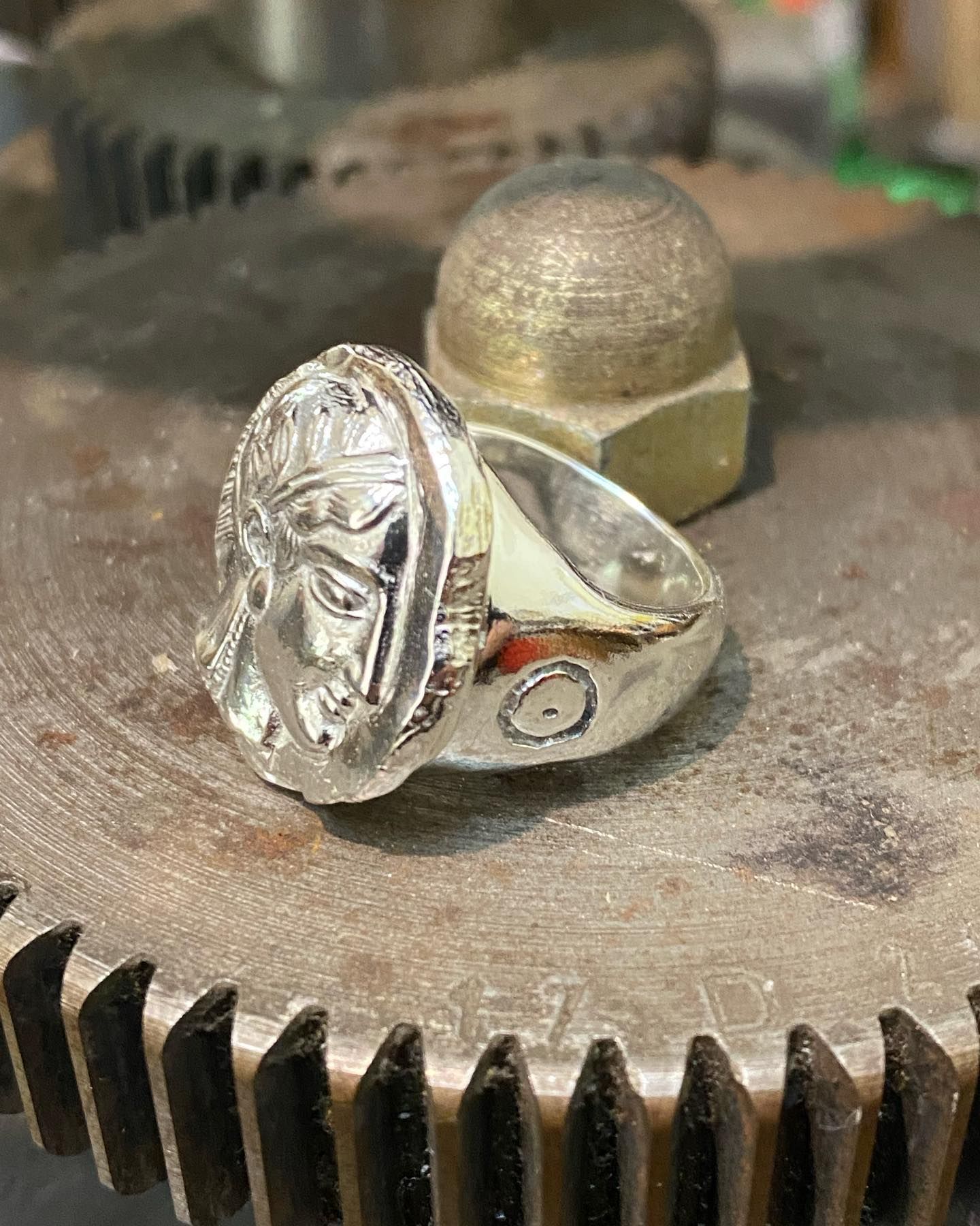 A silver ring with an embossed profile of a classical figure, resting on a metallic gear — Burchell's Jewellers In Bowral, NSW