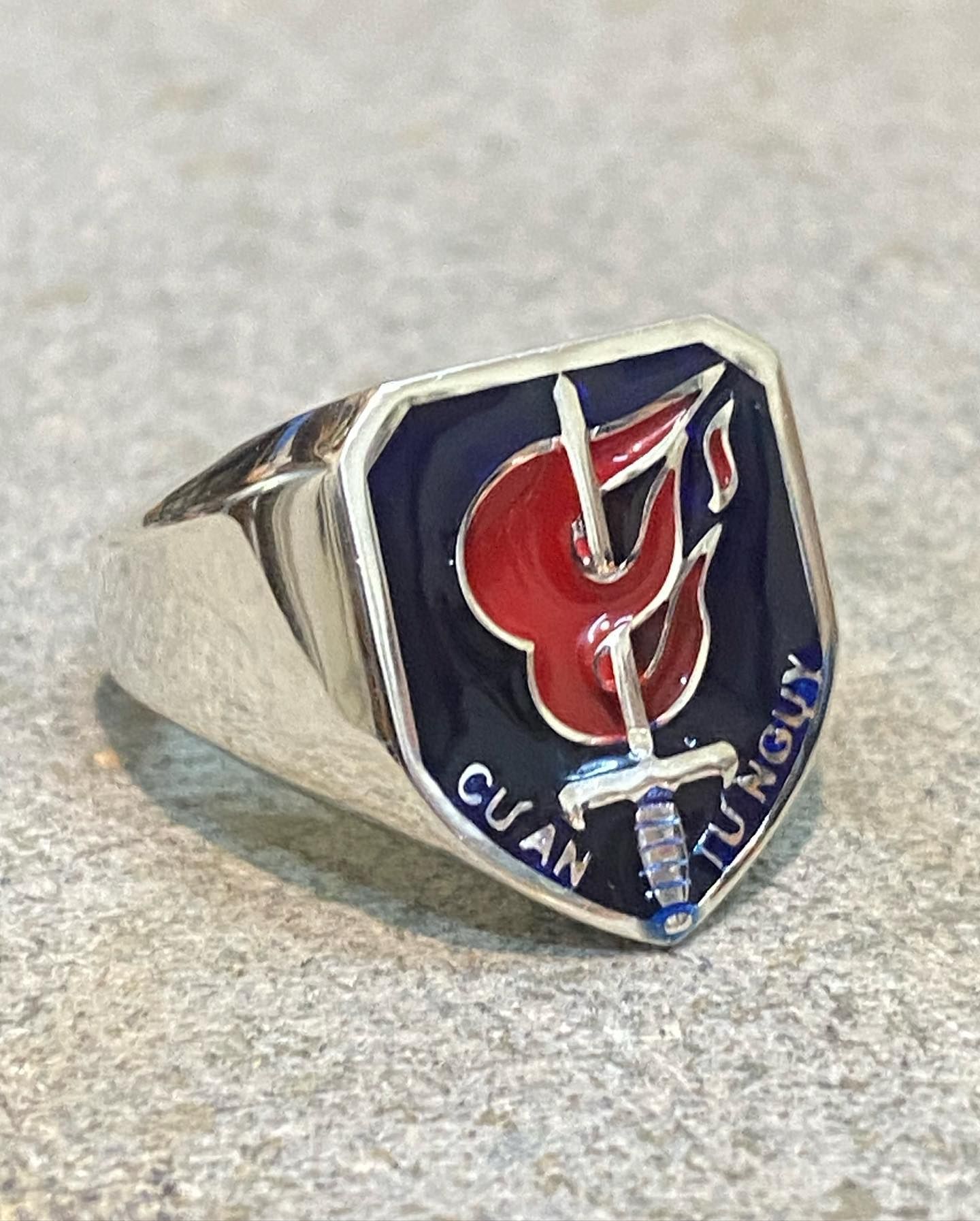 A silver ring featuring a blue shield crest with a central red flame pierced by a silver sword and the inscription — Burchell's Jewellers In Bowral, NSW