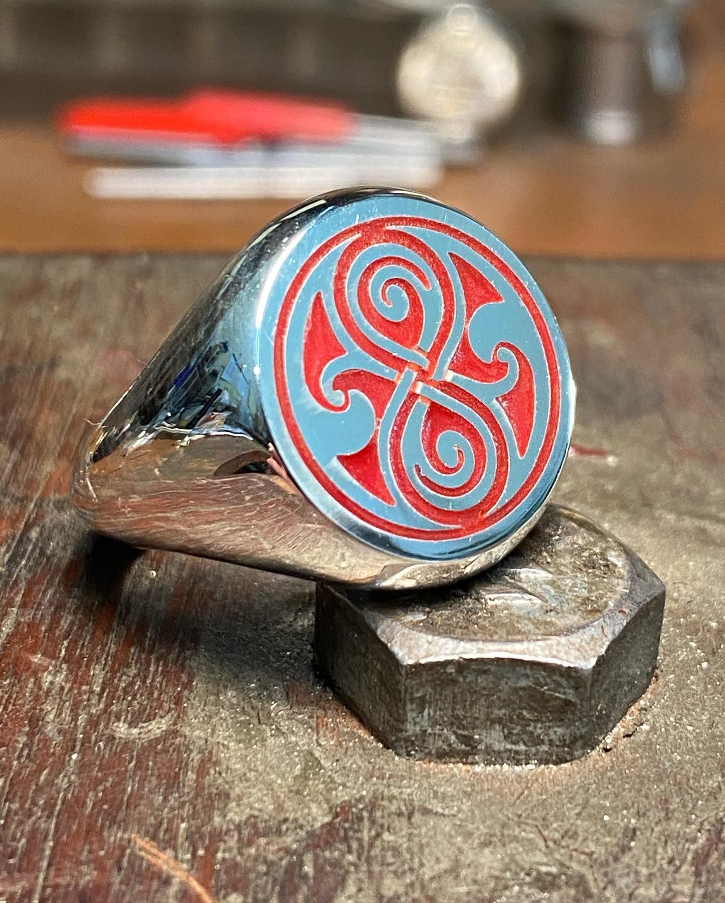 A silver signet ring with a red circular inlay featuring an engraved, symmetrical Celtic-inspired knot design — Burchell's Jewellers In Bowral, NSW