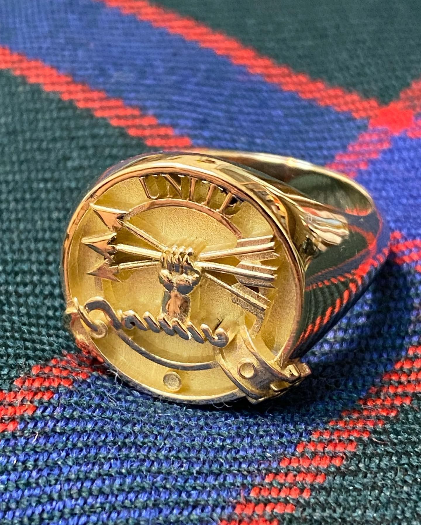 A gold ring with a crest featuring a hand gripping arrows and the word 