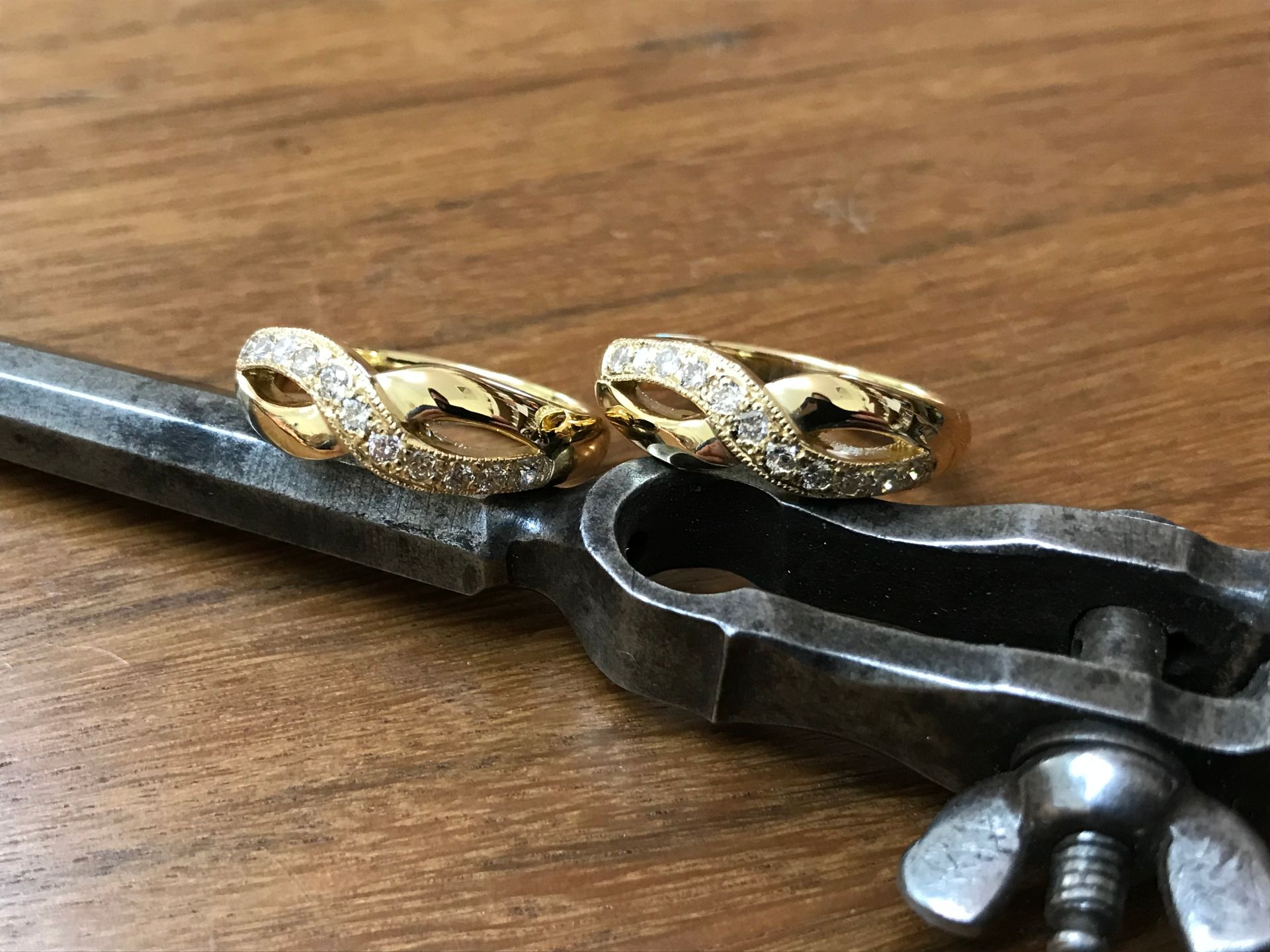 Two Gold Rings With Diamonds, Resting on a Silver Metal Tool, Set on a Wooden Surface — Burchell's Jewellers In Bowral, NSW