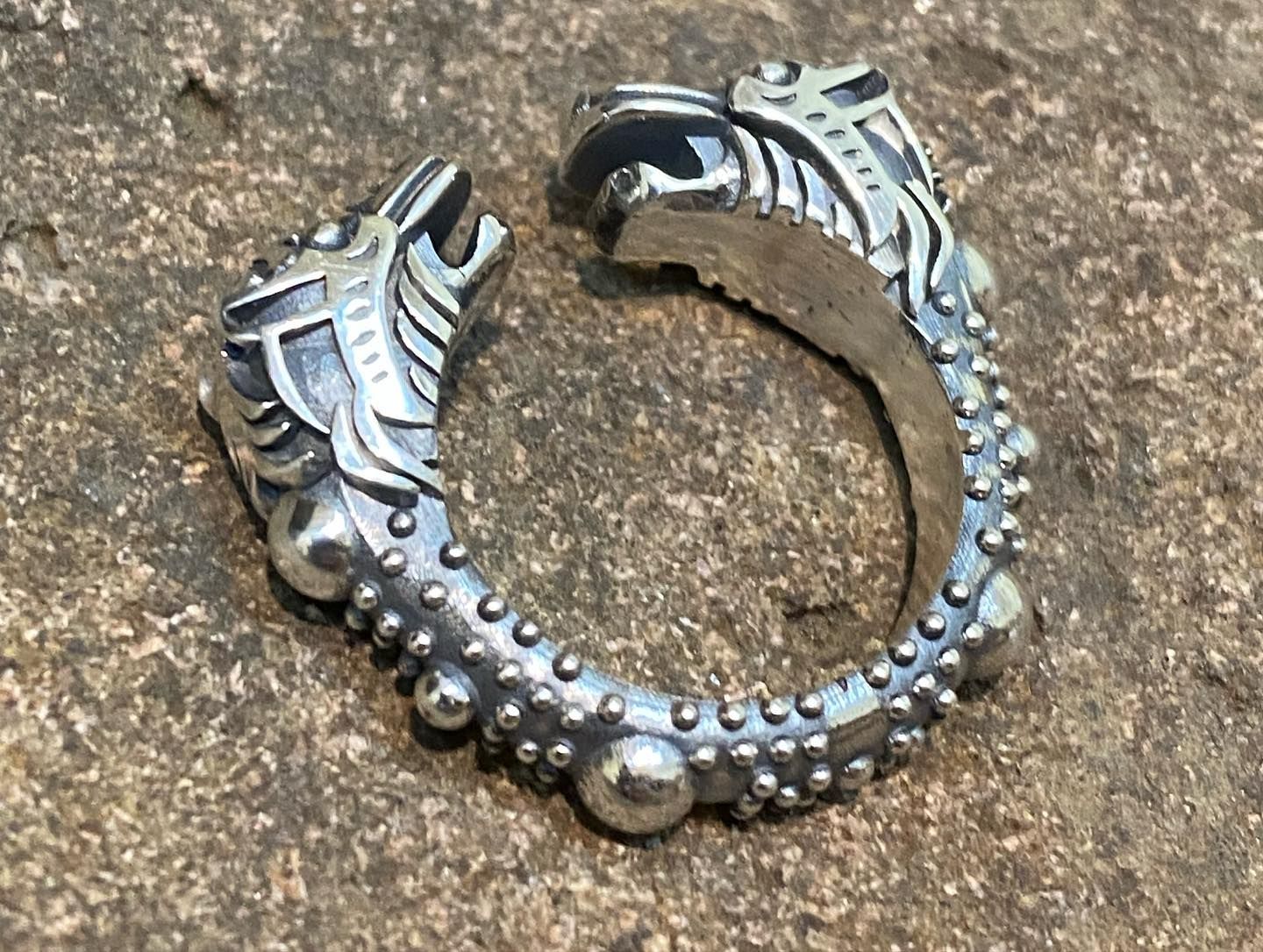 A silver Norse-style ring featuring two stylised wolf heads at the ends, textured with small metal studs, on stone — Burchell's Jewellers In Bowral, NSW