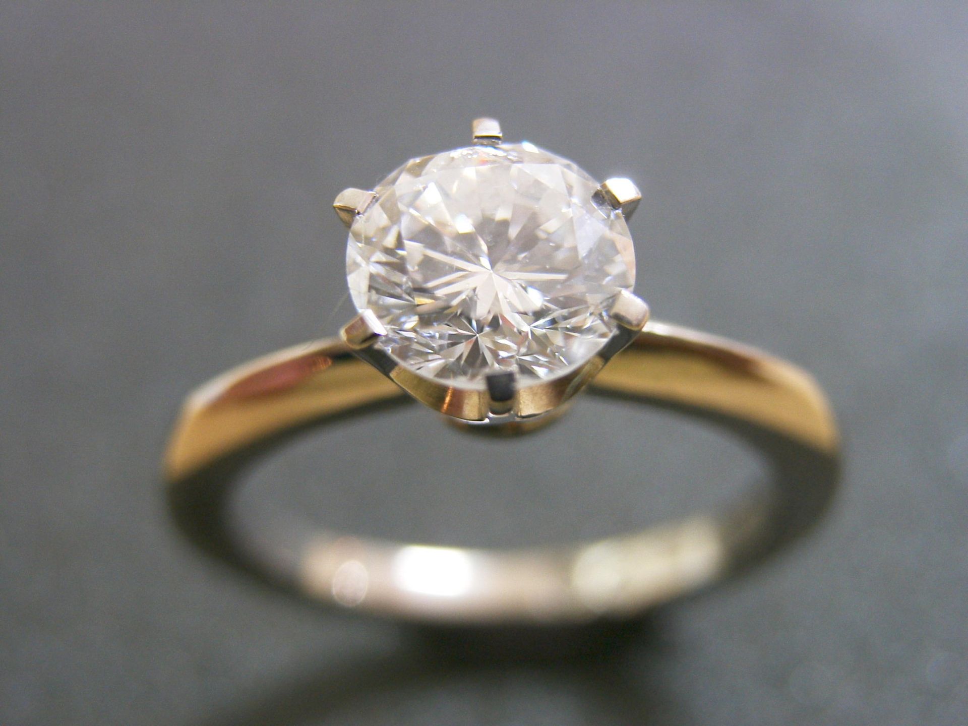 A solitaire diamond ring with a six-prong setting on a smooth, gold band against a dark background. — Burchell's Jewellers In Bowral, NSW