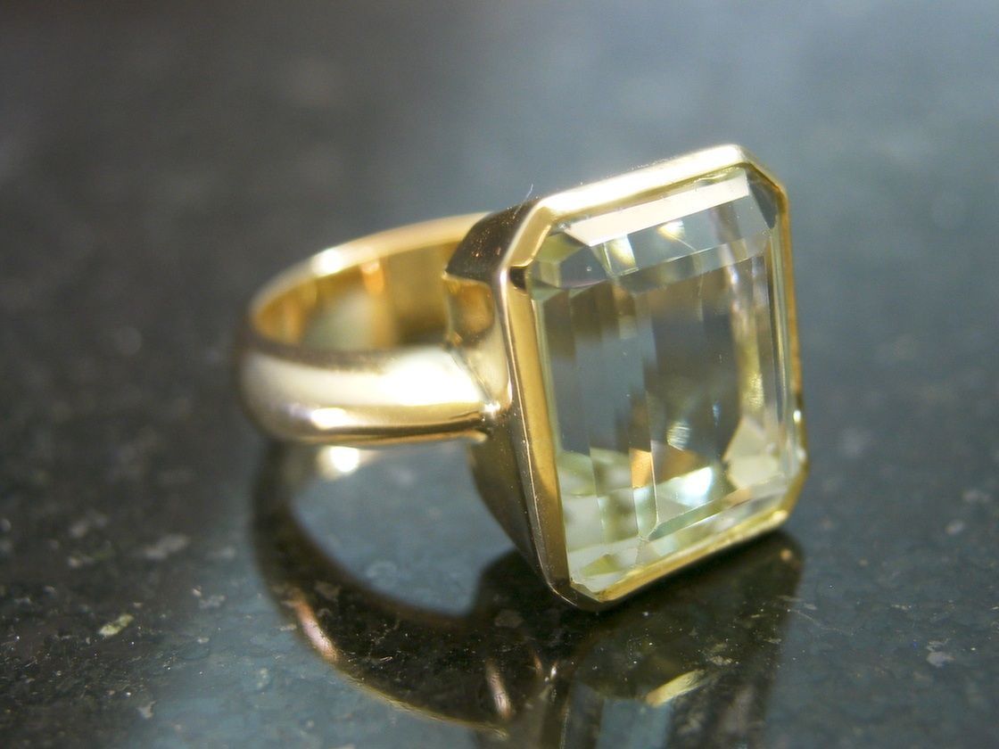 A gold ring featuring a large, rectangular-cut, pale yellow gemstone, resting on a dark, reflective surface. — Burchell's Jewellers In Bowral, NSW