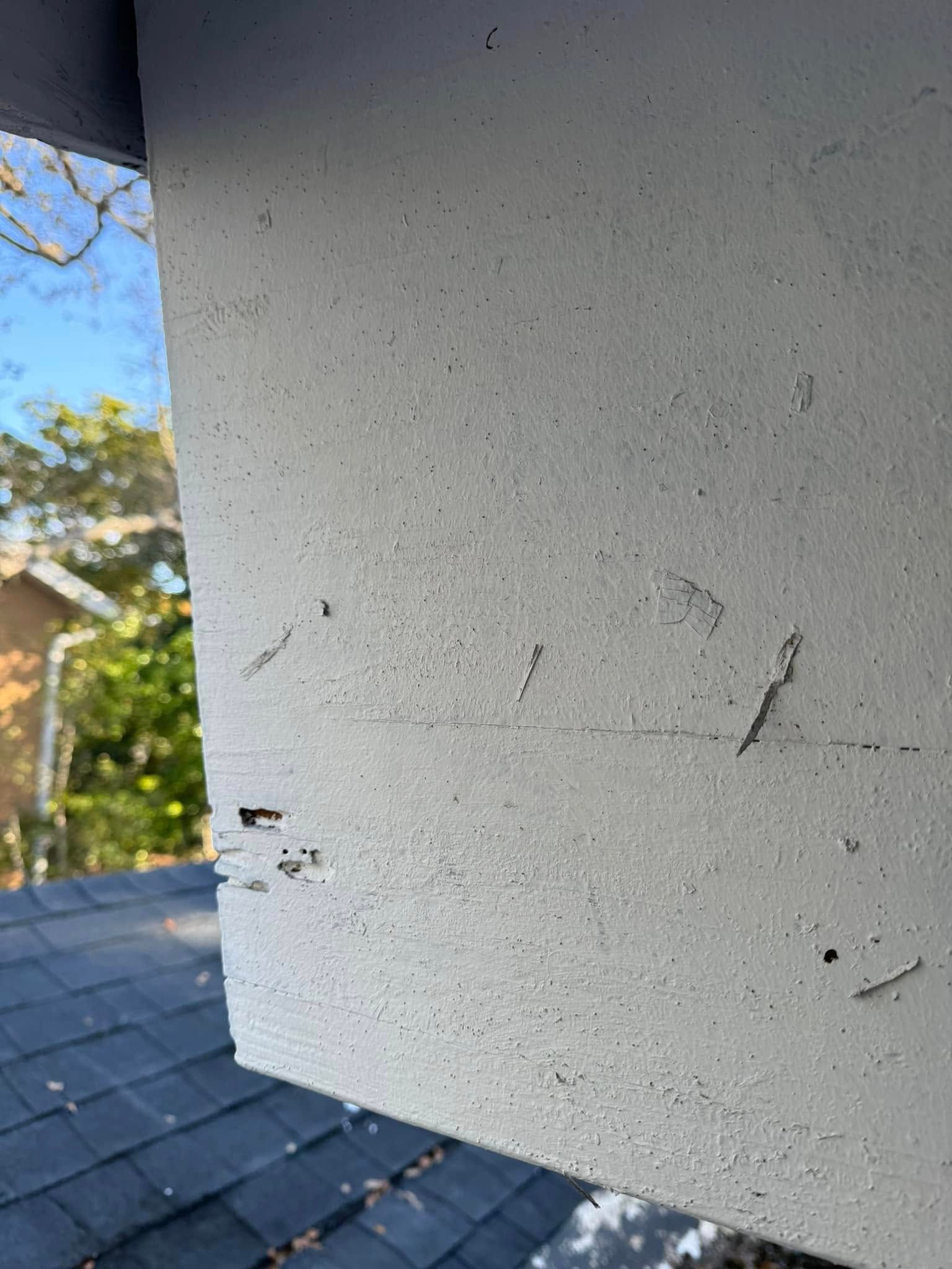 Close-up of a weathered, painted exterior wooden beam showing minor surface scuffs, scrapes, and small indentations.