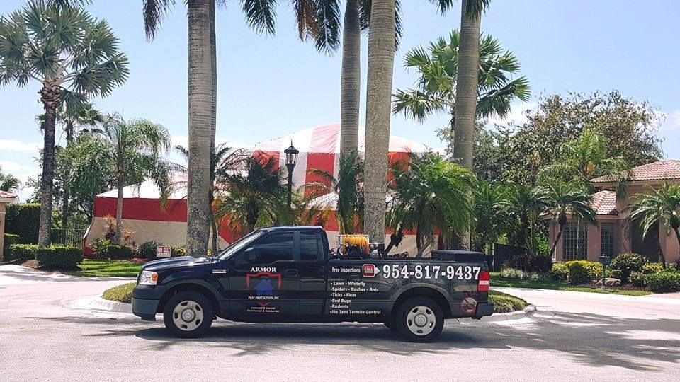 A black work truck parked on a paved driveway in front of a red-and-white striped event tent and palm trees.