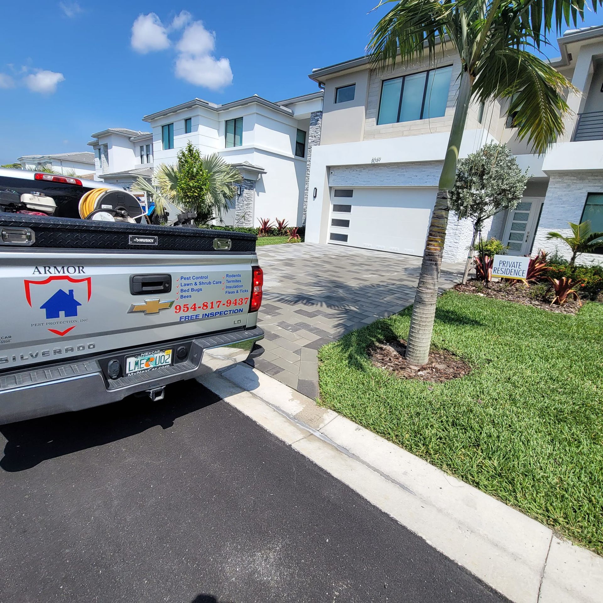 A silver Chevrolet work truck parked in front of modern, white multi-story townhomes on a sunny day.