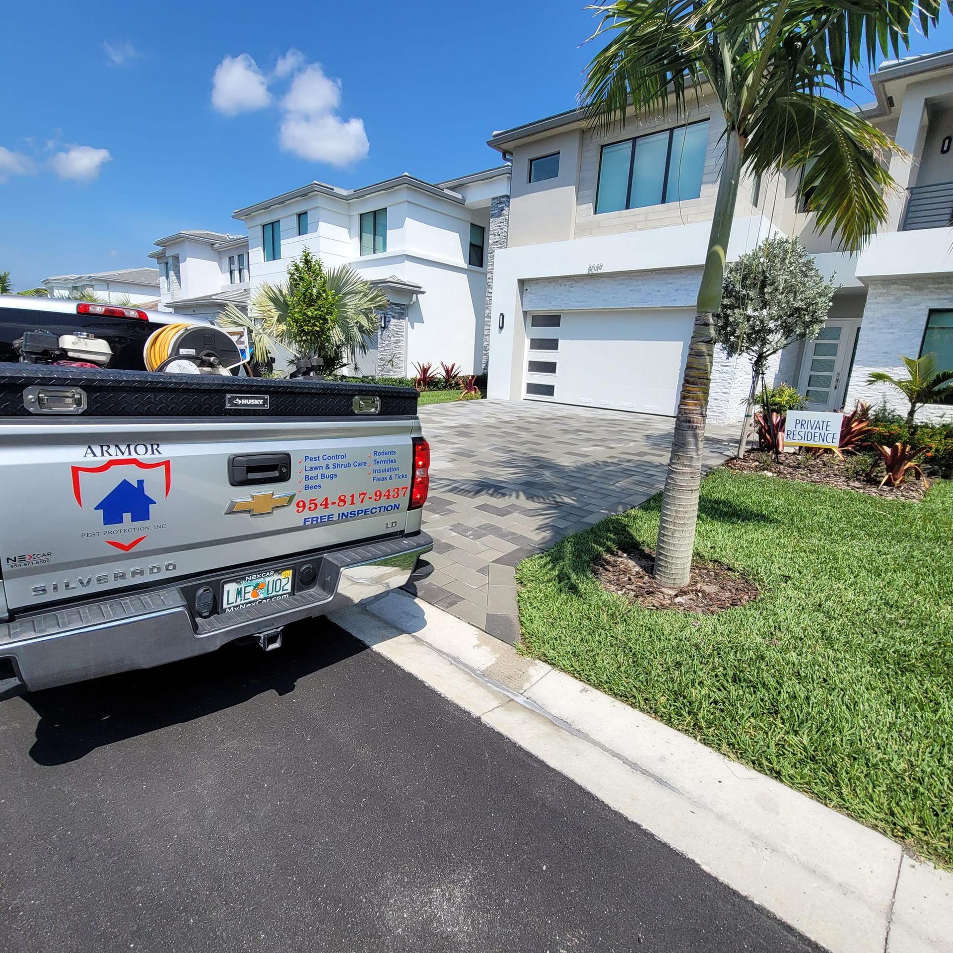 Silver pickup truck parked on a sunny street in front of modern, white residential townhouses with a manicured lawn.