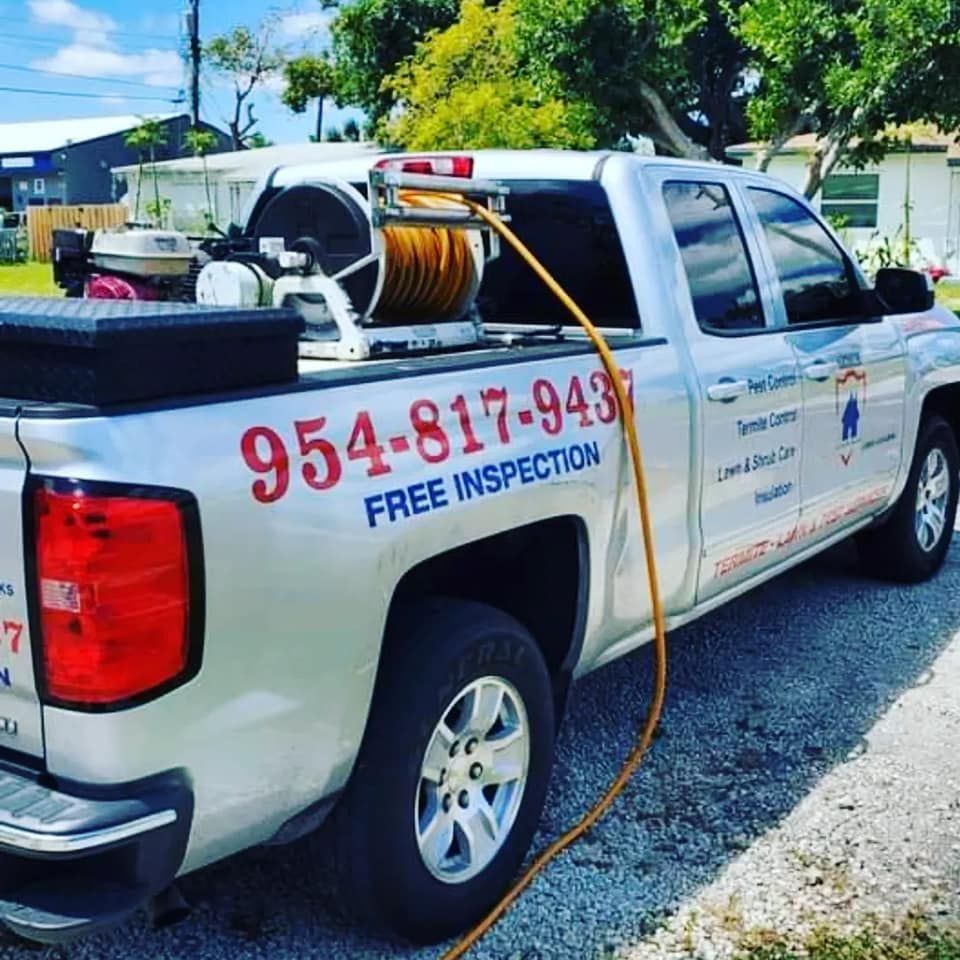 A silver service truck parked on gravel, featuring a hose reel and the phone number 954-817-9437 for pest control services.