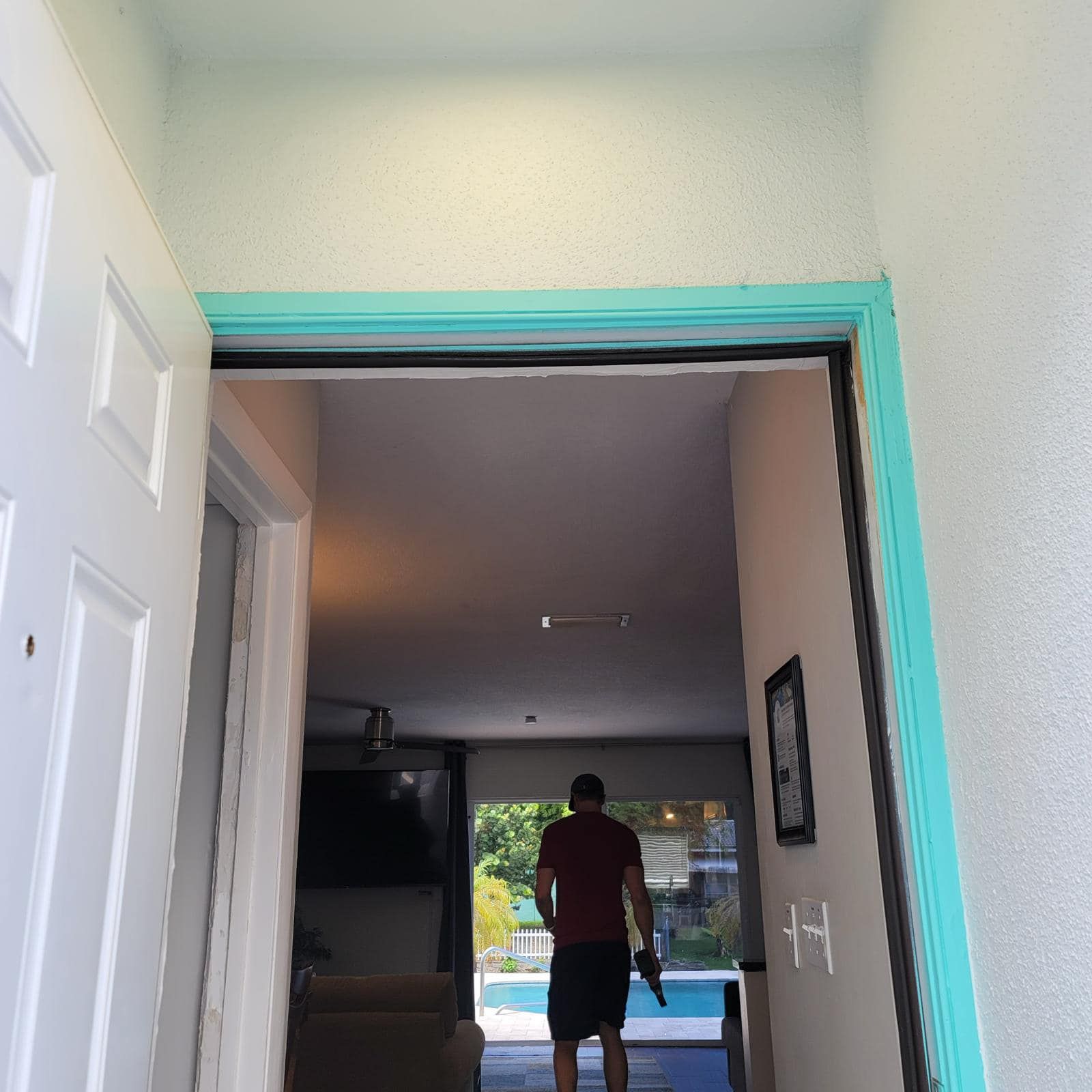 A person stands in a doorway looking toward a bright, sunlit living area that leads to a pool and backyard.