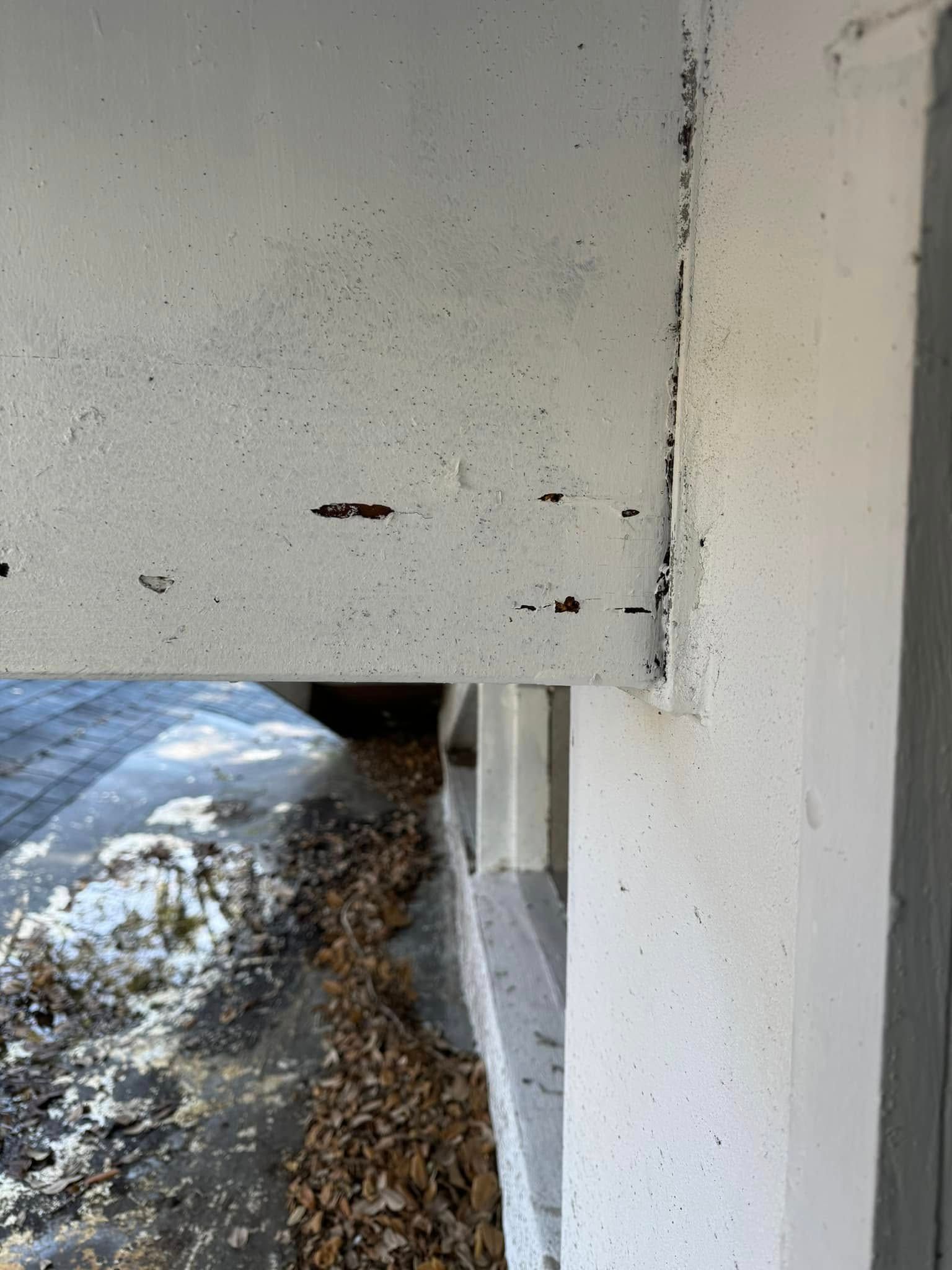 A close-up view of a white, exterior structural beam connected to a wall, showing paint chipping and debris on the ground.