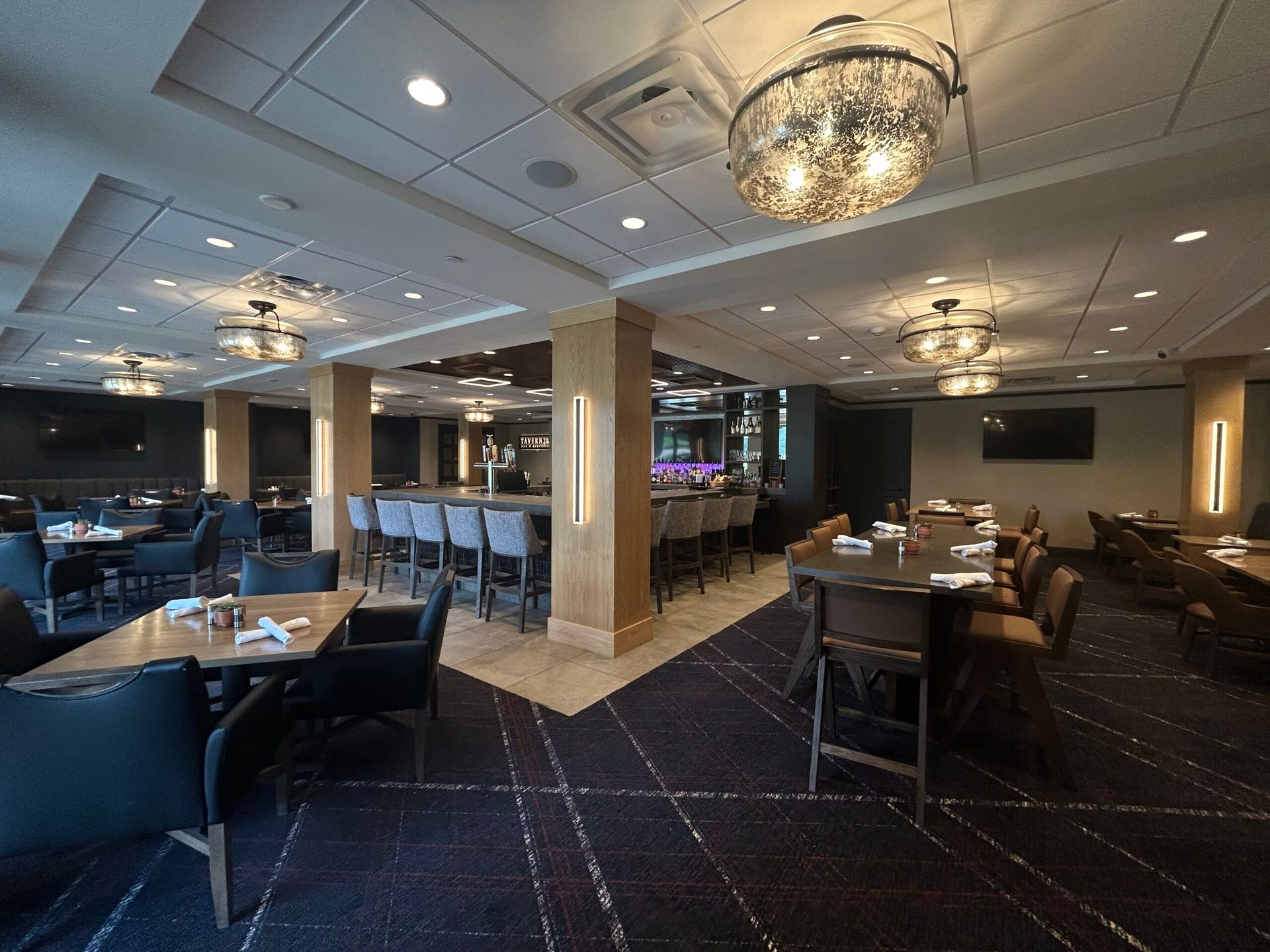 An upscale, dimly lit restaurant interior with tables, bar seating, dark carpets, and decorative globe chandeliers.