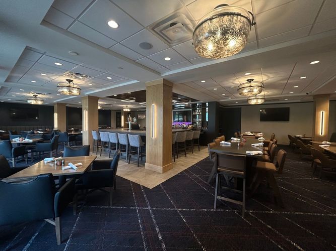 An upscale, dimly lit restaurant interior with tables, bar seating, dark carpets, and decorative globe chandeliers.