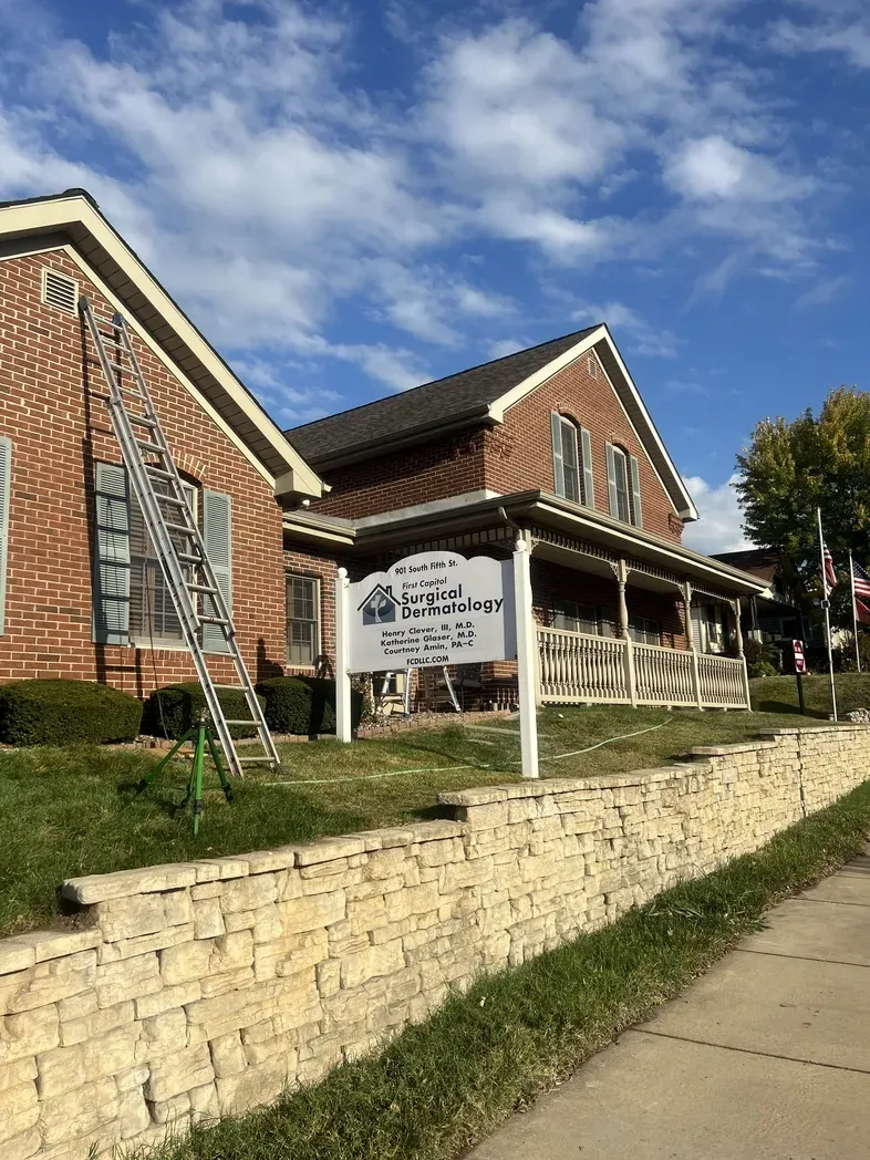A brick building with a porch and sign, featuring a tall ladder leaning against the exterior wall on a sunny day.