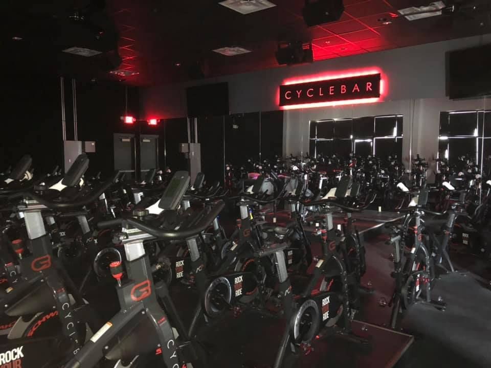 A CycleBar studio filled with rows of stationary exercise bikes under dim red lighting, featuring a glowing brand sign.